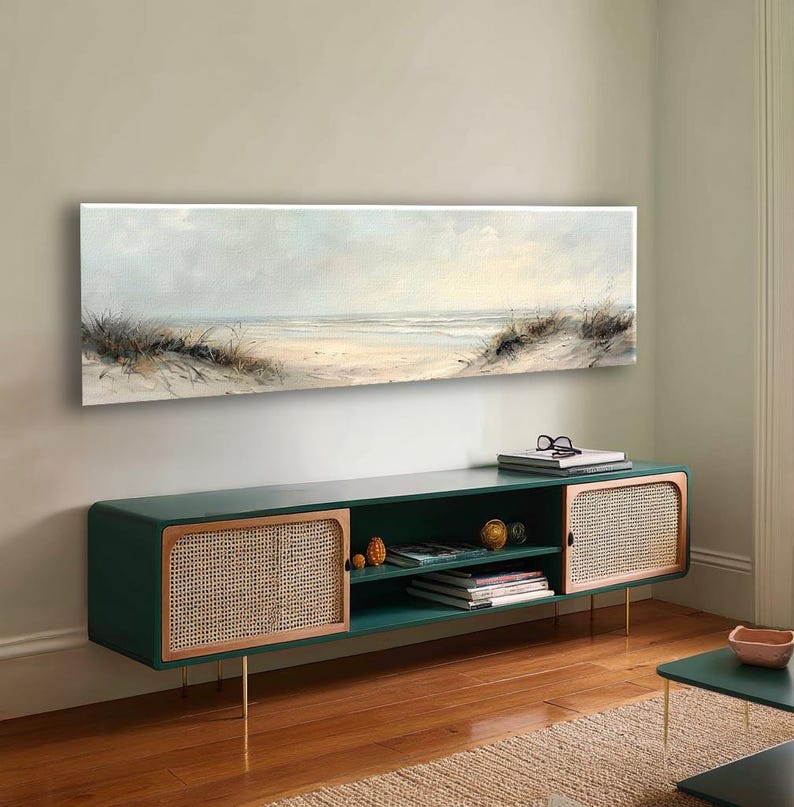 May include: A long, rectangular landscape painting depicting a coastal beach scene with soft, muted tones of beige, white, and pale blue. The artwork features sand dunes with tall grasses in the foreground and a calm ocean horizon in the distance.