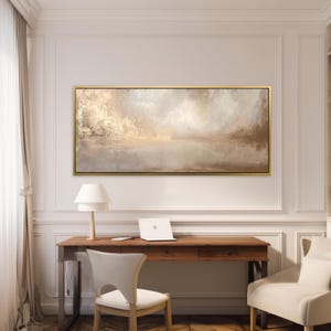 May include: An abstract landscape painting in a gold frame. The artwork features a blend of beige, brown, and white hues, creating a serene and neutral colour palette. The painting is displayed above a wooden desk with a laptop and lamp.