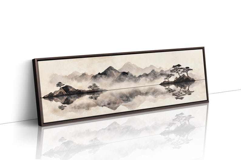 May include: A framed landscape art print featuring a serene mountain scene reflected in calm water. The artwork uses muted tones of gray, black, and beige, with stylized trees and mountains. The frame is dark brown.