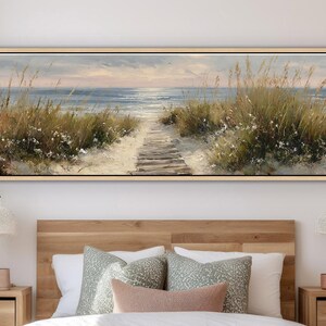 May include: A panoramic landscape painting in a light wood frame depicting a sandy beach path leading to the ocean. The scene features tall green dune grasses, white flowers, and a calm sea under a soft, muted sky at sunrise or sunset.