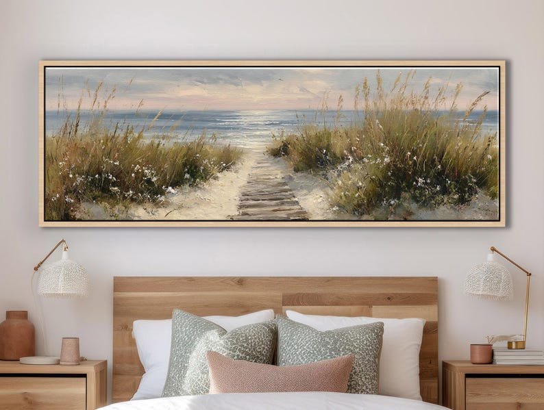 May include: A panoramic landscape painting in a light wood frame depicting a sandy beach path leading to the ocean. The scene features tall green dune grasses, white flowers, and a calm sea under a soft, muted sky at sunrise or sunset.