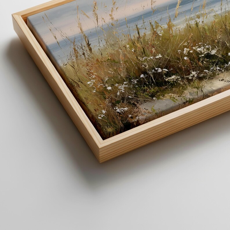May include: A framed canvas print featuring an impressionistic landscape painting of coastal dunes with tall golden grasses and small white wildflowers under a soft sky, encased in a light-toned wooden frame with a visible grain texture.