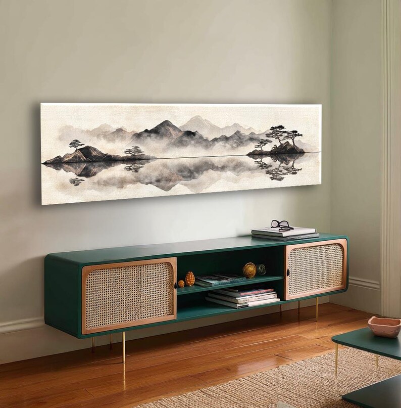 May include: A long, rectangular landscape painting depicts a serene mountain scene in shades of gray and white, with a reflective lake. Below, a dark green cabinet with woven rattan doors and gold legs adds a touch of modern design.
