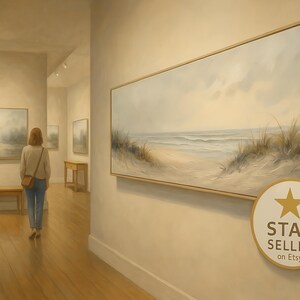 May include: An art gallery interior featuring a woman viewing a large framed landscape painting of a beach scene. The painting has a neutral color palette with a sandy beach, ocean waves, and tall grasses. The gallery has light-colored walls and wooden floors.