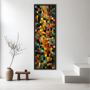 以下が含まれることがあります： 縦長の長方形のフレームに入った抽象芸術作品。赤、黄、緑、青の色合いのカラフルな正方形のモザイクが特徴です。絵画は白い壁に展示されており、手前に小さな木製のテーブルと植物が入った花瓶があります。