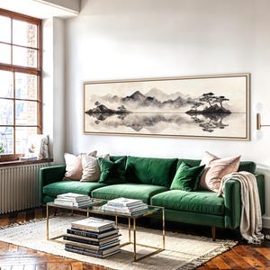 May include: A living room scene featuring a large landscape painting above a green velvet sofa. The painting depicts a serene mountain and lake scene in muted tones. Two glass-top coffee tables with gold frames sit on a rug.