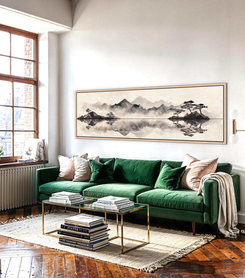 May include: A living room scene featuring a large landscape painting above a green velvet sofa. The painting depicts a serene mountain and lake scene in muted tones. Two glass-top coffee tables with gold frames sit on a rug.