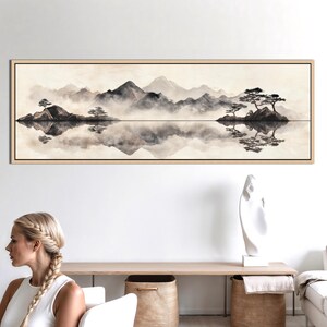 May include: A framed landscape art print featuring a serene mountain scene with a lake reflection. The artwork is in shades of gray and beige, with trees and mountains. The artwork is in a rectangular shape.