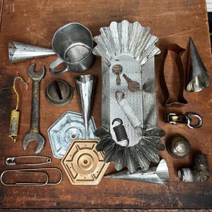 May include: A collection of assorted metal objects including a fluted rectangular baking pan, a silver mug, metal cones, a wrench, a spring, a safety pin, a paperclip, a copper penguin cookie cutter, a pulley, and various hardware components.