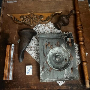 May include: A collection of vintage architectural elements including a carved wooden pediment, a dark wood finial, a curved furniture leg, a weathered gray painted block with a circular medallion, a long wooden spindle, and a white mahjong tile.