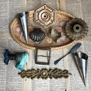 May include: A collection of vintage metal objects including a brass hexagonal fastener, a silver shell mold, a Texas-shaped cookie cutter, a brass floral candle holder, a blue faucet handle, a metal buckle, a decorative brass plate, and two metal cones.