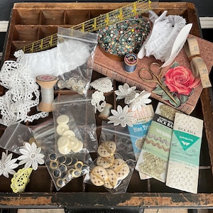 May include: A wooden drawer organizer filled with various sewing supplies, including lace, buttons, spools of thread, a pincushion, and a pair of scissors. There are also several packages of trim and ribbon.