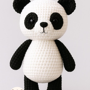 Può includere: Un peluche di orso panda all'uncinetto fatto a mano. Il panda ha un corpo bianco con dettagli neri su orecchie, braccia e gambe. Ha occhi neri e un piccolo naso nero. Il peluche è in piedi.