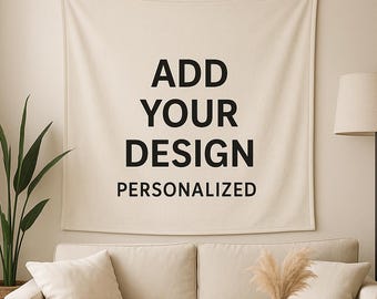 Op de afbeelding: Een crèmekleurige wandophanging met de tekst "ADD YOUR DESIGN PERSONALIZED" in het zwart. De wandophanging wordt weergegeven boven een beige bank met bijpassende kussens. Een ronde houten salontafel en een plant in pot staan op de voorgrond.