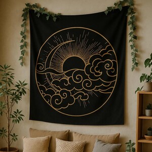 Könnte beinhalten: Schwarzes Wandtuch mit goldenem Sonnen- und Wolkenmuster. Es hängt über einem beigen Sofa mit Zierkissen. Ein runder Holztisch und Pflanzen ergänzen die Raumdekoration.