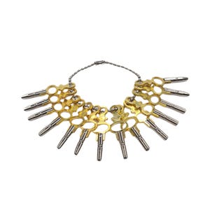 Op de afbeelding: Een ketting met een reeks sleutels in antieke stijl. De sleutels zijn goudkleurig met zilverkleurige stelen, verbonden door een zilveren ketting. De sleutels zijn in een waaier op een witte achtergrond gerangschikt.