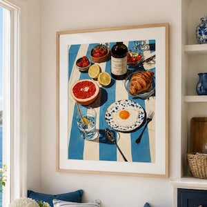 May include: A framed print shows a breakfast scene with a blue and white striped tablecloth. The image includes a grapefruit, strawberries, a croissant, a fried egg, and a bottle of wine. A glass of water and a blue and white patterned plate are also visible.