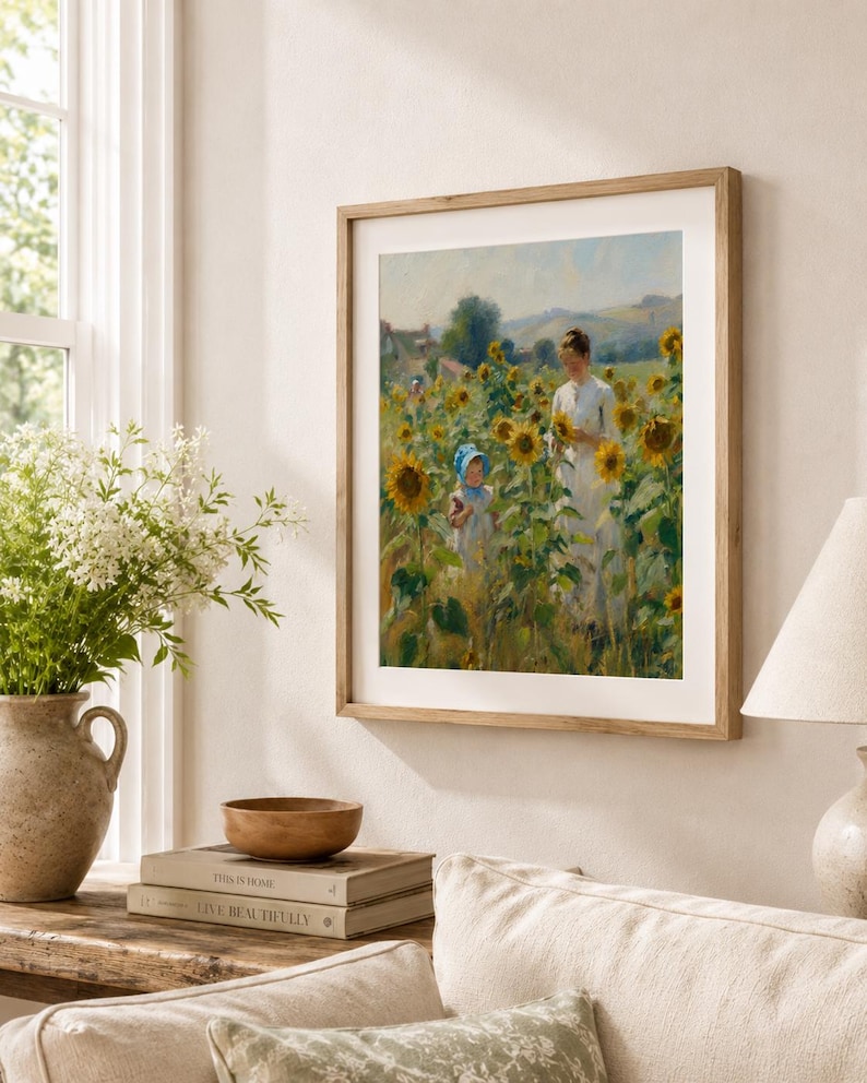 Puede incluir: Una impresi&oacute;n enmarcada de una pintura que representa a una mujer y un ni&ntilde;o en un campo de girasoles. La obra de arte est&aacute; en un marco de madera y cuelga de una pared beige. Un jarr&oacute;n con flores blancas y libros est&aacute;n sobre una mesa de madera debajo.