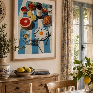May include: A framed print shows a breakfast setting with a blue and white striped cloth. It includes a wine bottle, croissant, grapefruit, strawberries, lemons, and a fried egg on a plate. The print hangs above a wooden cabinet, with a bowl of lemons.