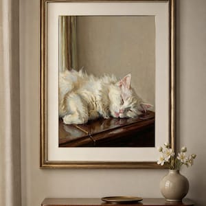 May include: A framed painting depicting a white cat asleep on a dark wooden surface. The artwork is in a gold frame, displayed above a wooden chest of drawers. A small vase with white flowers and a gold plate are on the chest.