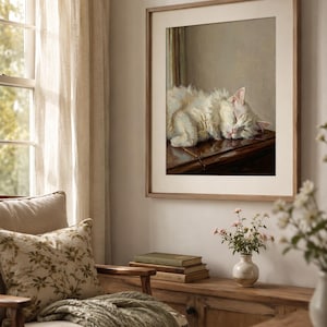 May include: A framed print depicting a sleeping white cat with pink ears. The artwork is in a light brown wooden frame. The room features a wooden cabinet, a chair with a floral pillow, and a window with sheer curtains. The image is in a room.