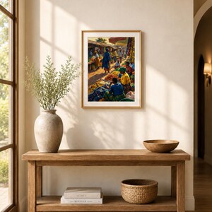 May include: A framed print showing a bustling outdoor market with figures in bright attire. The artwork hangs above a wooden console table, adorned with a vase of foliage, books, a woven basket, and a wooden bowl.