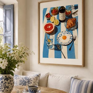 May include: A framed print depicting a breakfast scene with a blue and white striped tablecloth. The print includes a bottle of wine, a croissant, a grapefruit, strawberries, and a fried egg on a plate. A vase of white flowers and a table setting are in the foreground.