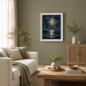 May include: A framed painting depicts a moonlit ocean scene with dark blue waves and a bright moon. The artwork hangs on an olive green wall in a living room setting. A white sofa with green pillows and a blanket, a wooden coffee table, and a woven rug complete the scene.