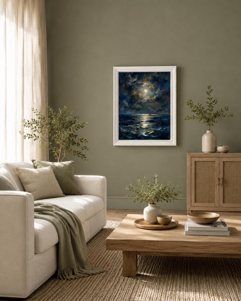 May include: A framed painting depicts a moonlit ocean scene with dark blue waves and a bright moon. The artwork hangs on an olive green wall in a living room setting. A white sofa with green pillows and a blanket, a wooden coffee table, and a woven rug complete the scene.