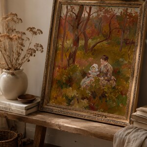 May include: An antique framed painting depicts a woman and child in a forest scene with autumn colors. The painting has a gold ornate frame and is displayed on a rustic wooden bench. A vase of dried flowers and books are next to the painting.