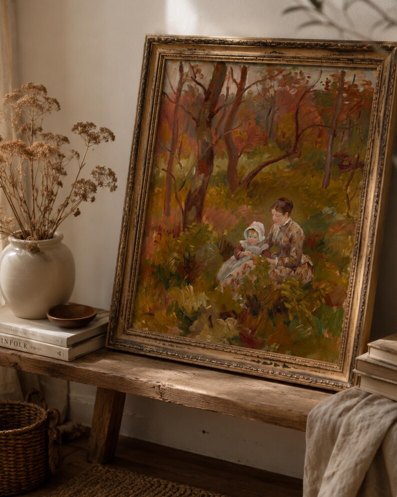 May include: An antique framed painting depicts a woman and child in a forest scene with autumn colors. The painting has a gold ornate frame and is displayed on a rustic wooden bench. A vase of dried flowers and books are next to the painting.
