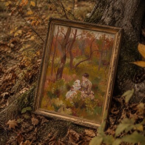 May include: An antique framed painting depicting a woman and child in a forest setting. The artwork features warm tones of brown, orange, and green, with a gold-colored frame. The painting is leaning against a tree trunk, surrounded by fallen leaves.