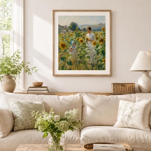 Puede incluir: Un cuadro enmarcado representa a una mujer y un ni&ntilde;o en un campo de girasoles. La obra de arte, en tonos c&aacute;lidos, se exhibe sobre un sof&aacute; beige con cojines. Una mesa de centro de madera sostiene un jarr&oacute;n con flores blancas y una bandeja tejida.