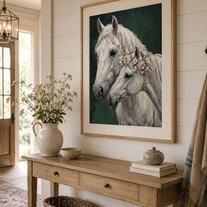 Op de afbeelding: Een ingelijste kunstdruk met twee witte paarden, waarvan &eacute;&eacute;n met een bloemenkrans, tegen een donkergroene achtergrond. Het kunstwerk hangt boven een houten console met een vaas bloemen, een kom en een rieten mand.