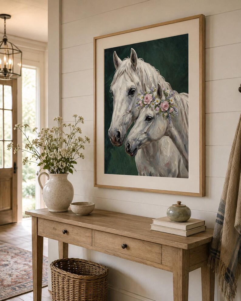 Op de afbeelding: Een ingelijste kunstdruk met twee witte paarden, waarvan &eacute;&eacute;n met een bloemenkrans, tegen een donkergroene achtergrond. Het kunstwerk hangt boven een houten console met een vaas bloemen, een kom en een rieten mand.