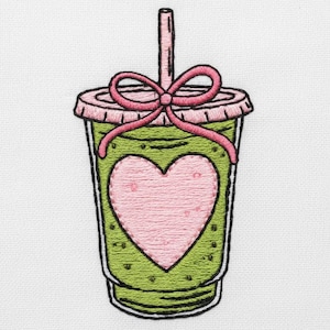 May include: Embroidered design of a green smoothie in a clear cup with a pink lid and bow. A pink heart is embroidered on the front of the cup. A straw extends from the top.