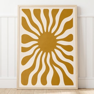 May include: A rectangular wall art print in a light wood frame featuring a mustard yellow sun graphic with wavy, radiating rays against a cream-colored background. The design consists of a central solid circle with elongated, curved shapes extending outward.