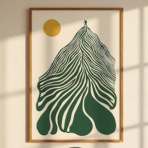 Puede incluir: Una impresión artística enmarcada con un diseño de montaña verde y blanca y un sol amarillo. Una pequeña figura está en la cima de la montaña. La impresión está en un marco de madera. Un jarrón verde y libros están en un mueble de madera.