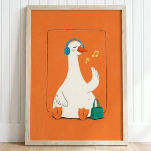 May include: A framed art print featuring a white goose with orange feet and beak, wearing blue headphones. The goose is sitting next to a small green handbag against a solid orange background. Two yellow musical notes float near the goose's head.