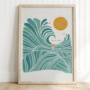 May include: A framed wall art print featuring a stylized teal and green ocean wave with a large yellow sun and small birds in the sky. The text "Dare to dream" is printed in the center of the wave. The frame is made of light-colored wood.