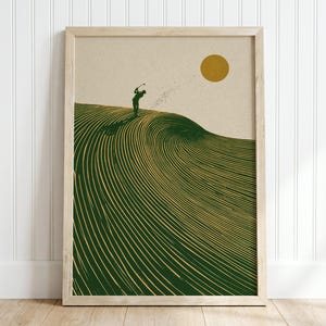 May include: A framed wall art print featuring a silhouette of a golfer swinging a club atop a large, stylised green wave with gold line details. A solid gold circle representing the sun is positioned in the upper right corner against a beige background.