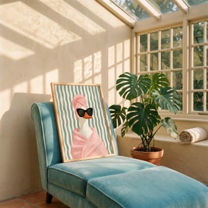 May include: A framed wall art print featuring a white duck wearing a pink towel wrap on its head and body, paired with black sunglasses. The background consists of vertical teal and white wavy stripes, all contained within a light wood frame.