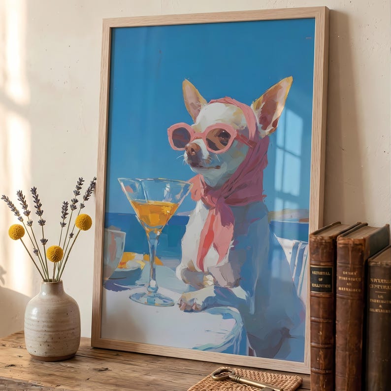 Puede incluir: Una impresi&oacute;n art&iacute;stica enmarcada representa un chihuahua blanco con gafas de sol y bufanda rosas, disfrutando de un c&oacute;ctel. El perro est&aacute; situado sobre un fondo de cielo azul y mar, con una copa de martini sobre una mesa. La obra est&aacute; en un marco de madera clara.