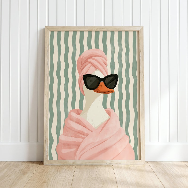May include: A framed wall art print featuring a white duck wearing black cat-eye sunglasses and a pink towel wrapped around its head and body. The background consists of a vertical wavy pattern in alternating shades of cream and sage green.