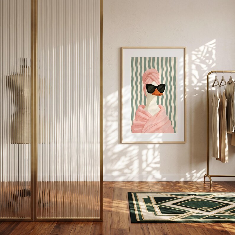 May include: A framed wall art print featuring a stylized illustration of a white duck wearing black sunglasses and a pink towel wrapped around its head and body, set against a background of vertical sage green and white wavy stripes.