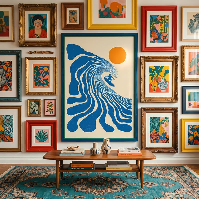 May include: A gallery wall featuring framed art prints in various sizes and styles. The central piece is a large blue and white wave print with a surfer. Other frames include abstract and figurative art, in gold, red, and blue frames. A wooden coffee table and a blue rug complete the scene.
