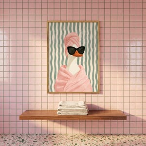 May include: A rectangular wall art print featuring a white duck wearing a pink towel wrapped around its head and body, paired with black cat-eye sunglasses. The background consists of vertical wavy teal and white stripes in a wooden frame.