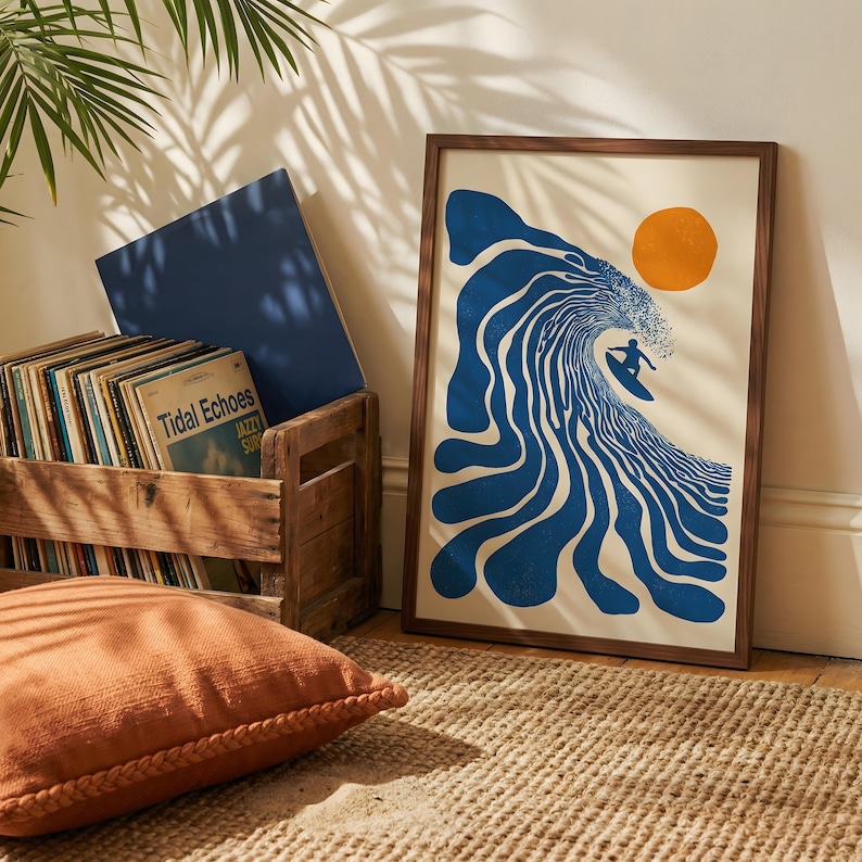 May include: A framed art print featuring a surfer riding a blue wave with an orange sun in the background. The print is in a wooden frame and is displayed on a woven rug. A wooden crate with vinyl records and a blue board are also in the image.