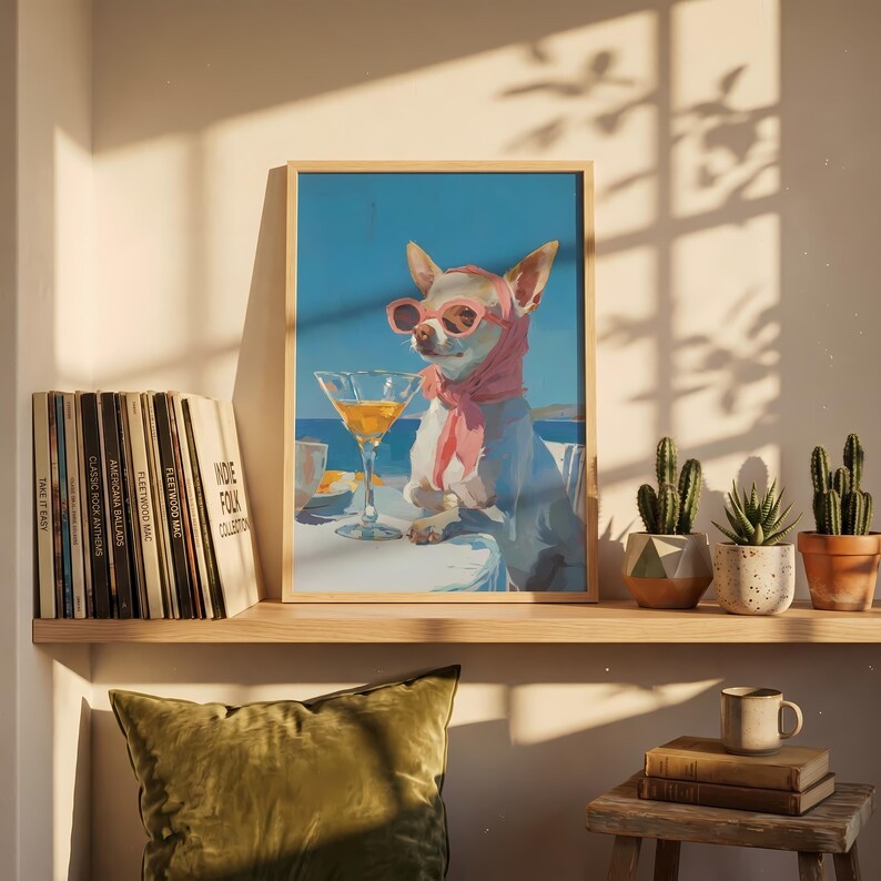 Puede incluir: Una impresi&oacute;n art&iacute;stica enmarcada representa a un chihuahua con gafas de sol rosas y una bufanda, disfrutando de un c&oacute;ctel. El perro est&aacute; sentado en una mesa con un fondo de oc&eacute;ano azul. La impresi&oacute;n se exhibe en un estante con discos de vinilo y cactus en macetas.