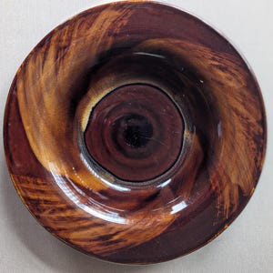 May include: A ceramic ashtray with a swirling design in shades of brown and tan. The center is a deep, dark brown, with lighter brown and tan brushstrokes radiating outwards. The ashtray has a glossy finish and a circular shape.